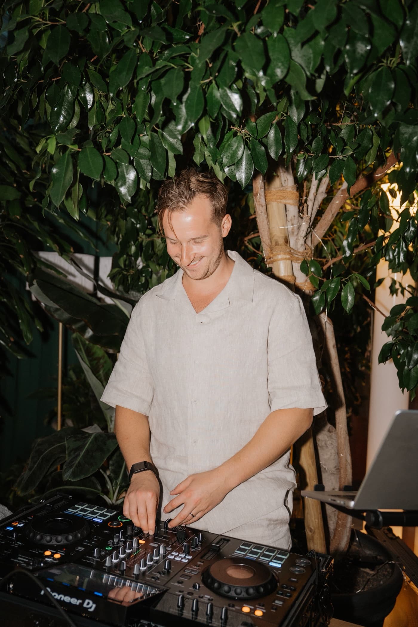 DJ Fedja lächelnd am Pioneer-DJ-Pult zwischen grünen Pflanzen